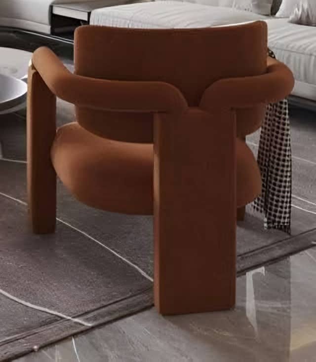 Sculptural armchair upholstered in terracotta fabric on a patterned rug